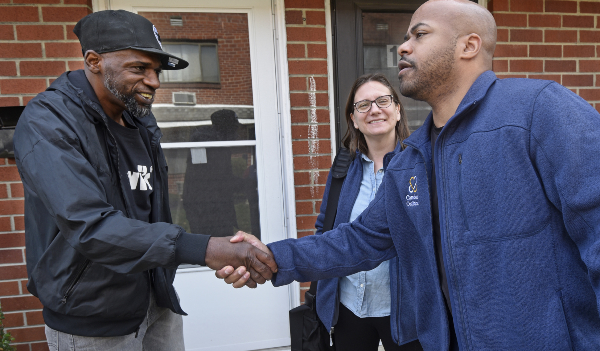 Camden Coalition care team member shakes hands with care management participant outside his apartment as a second care team member looks on